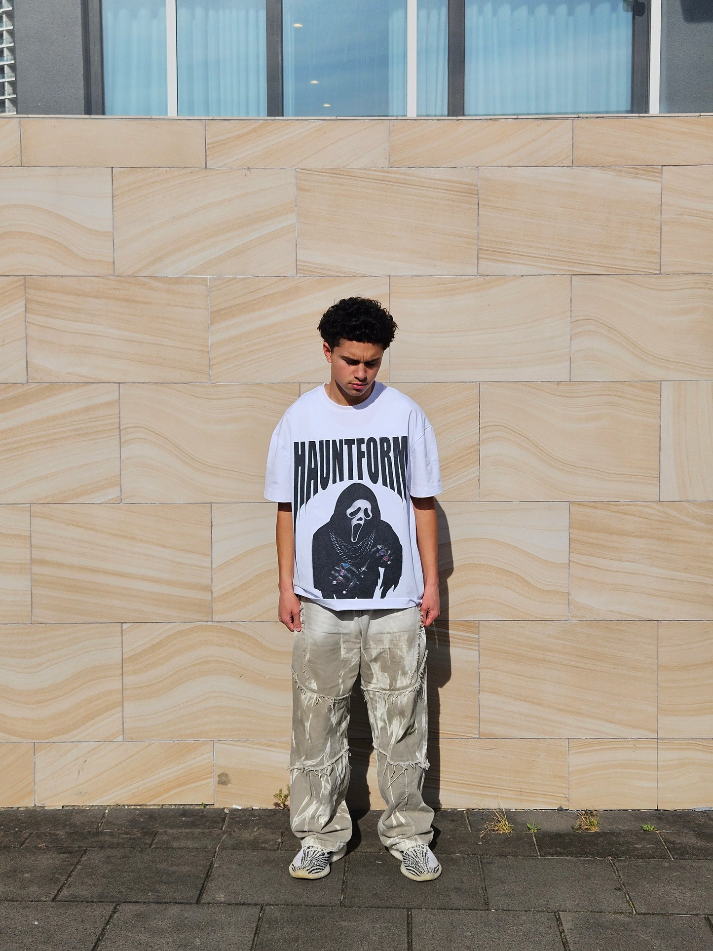 Person wearing a white t-shirt with a graphic design on a tiled pavement.
