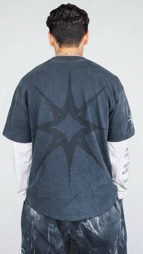 Person wearing a dark blue t-shirt with a star design, standing in front of a blackboard.