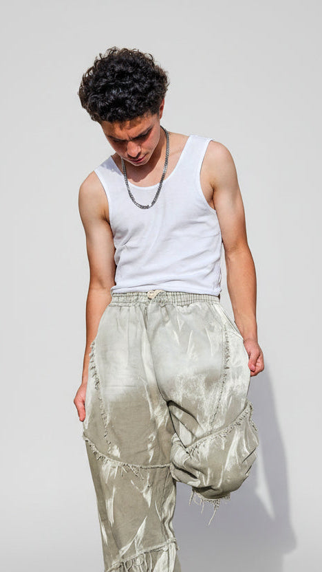 Person wearing a white tank top and light-colored pants against a stone wall.