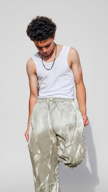 Person wearing a white tank top and light-colored pants against a stone wall.