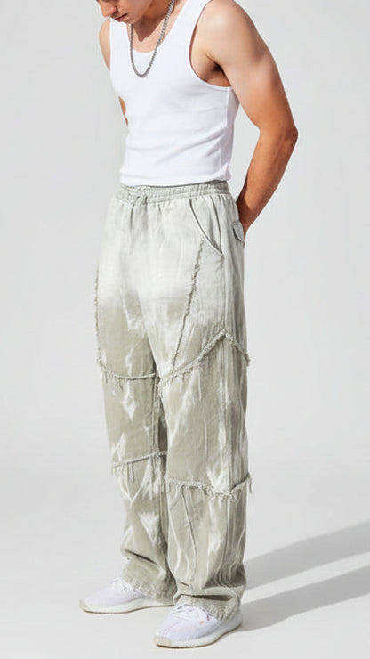 Person wearing a white tank top and light-colored pants leaning against a beige stone wall.